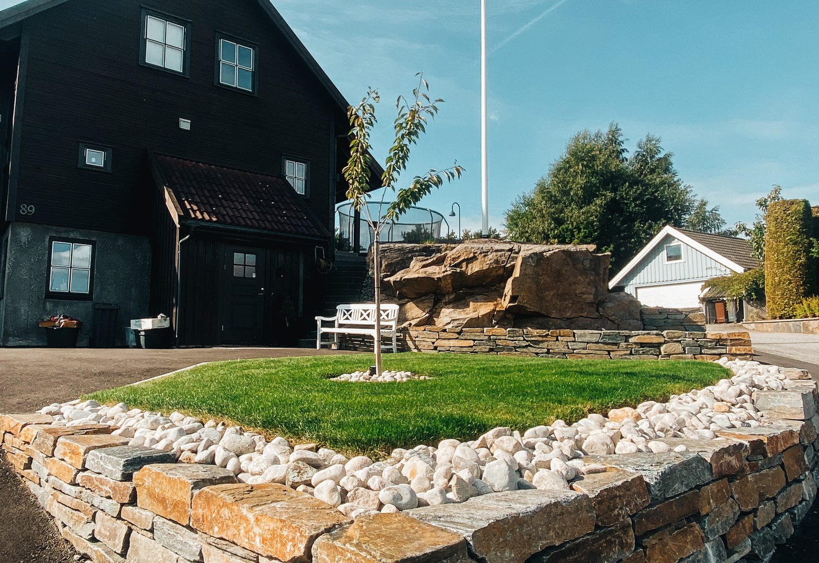 Buet natursteinsmur rundt plen med hvit singel og nyplantet tre